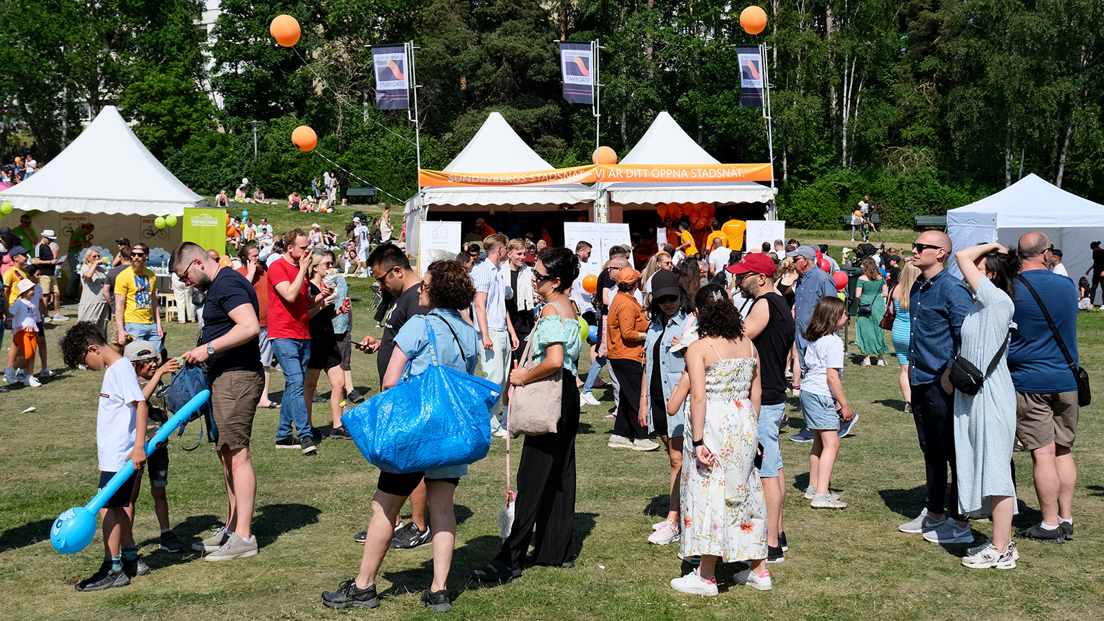 Parkmiljö med mycket folk, Sundbybergs stadsnät har ett stånd i bakgrunden.