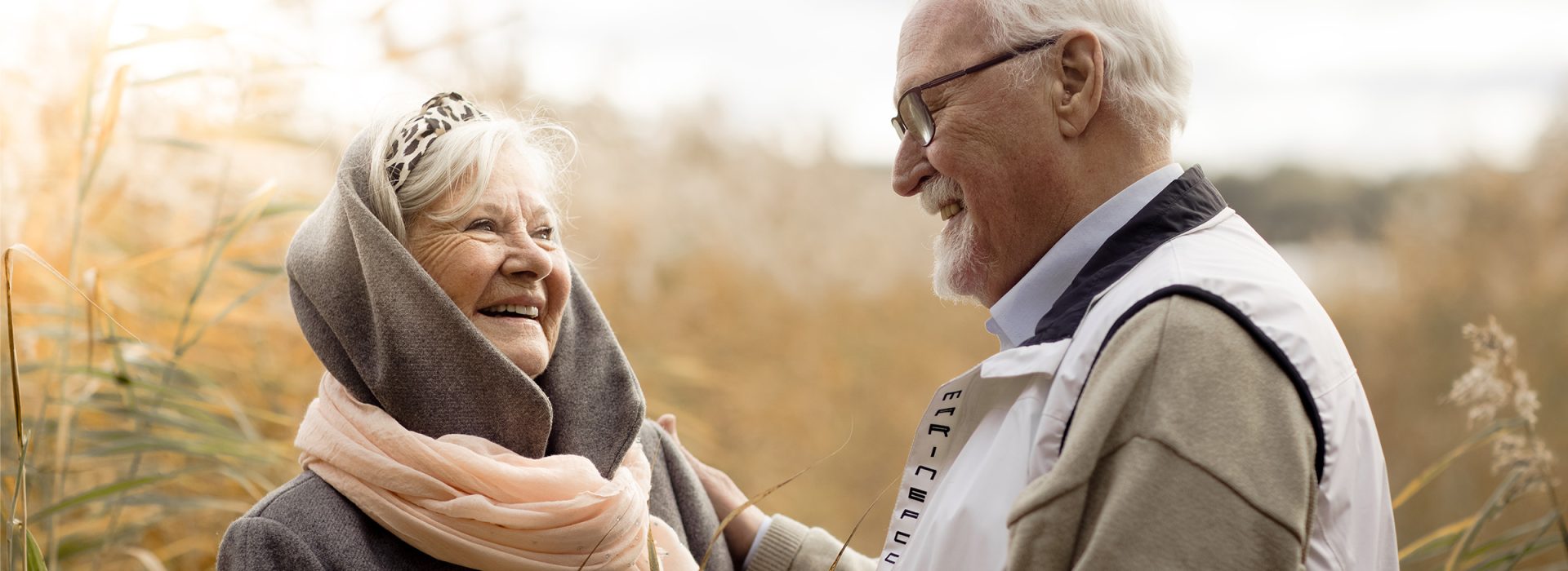 Äldre par som står i vass ute i naturen och ser glada ut