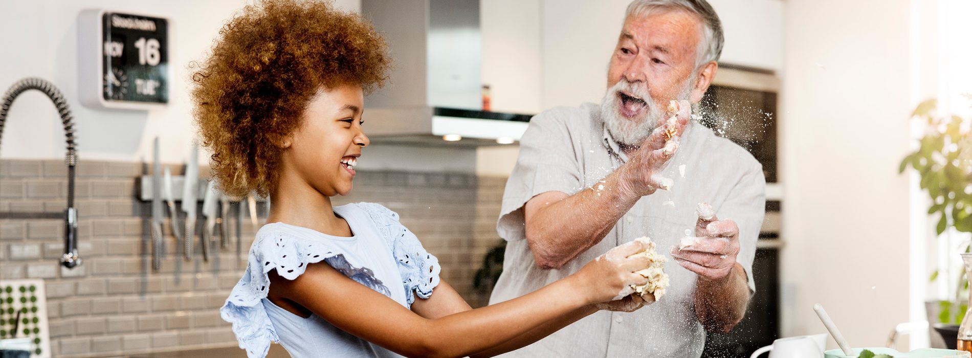 Äldre man som bakar med flicka så mjölet stänker och ser glada ut